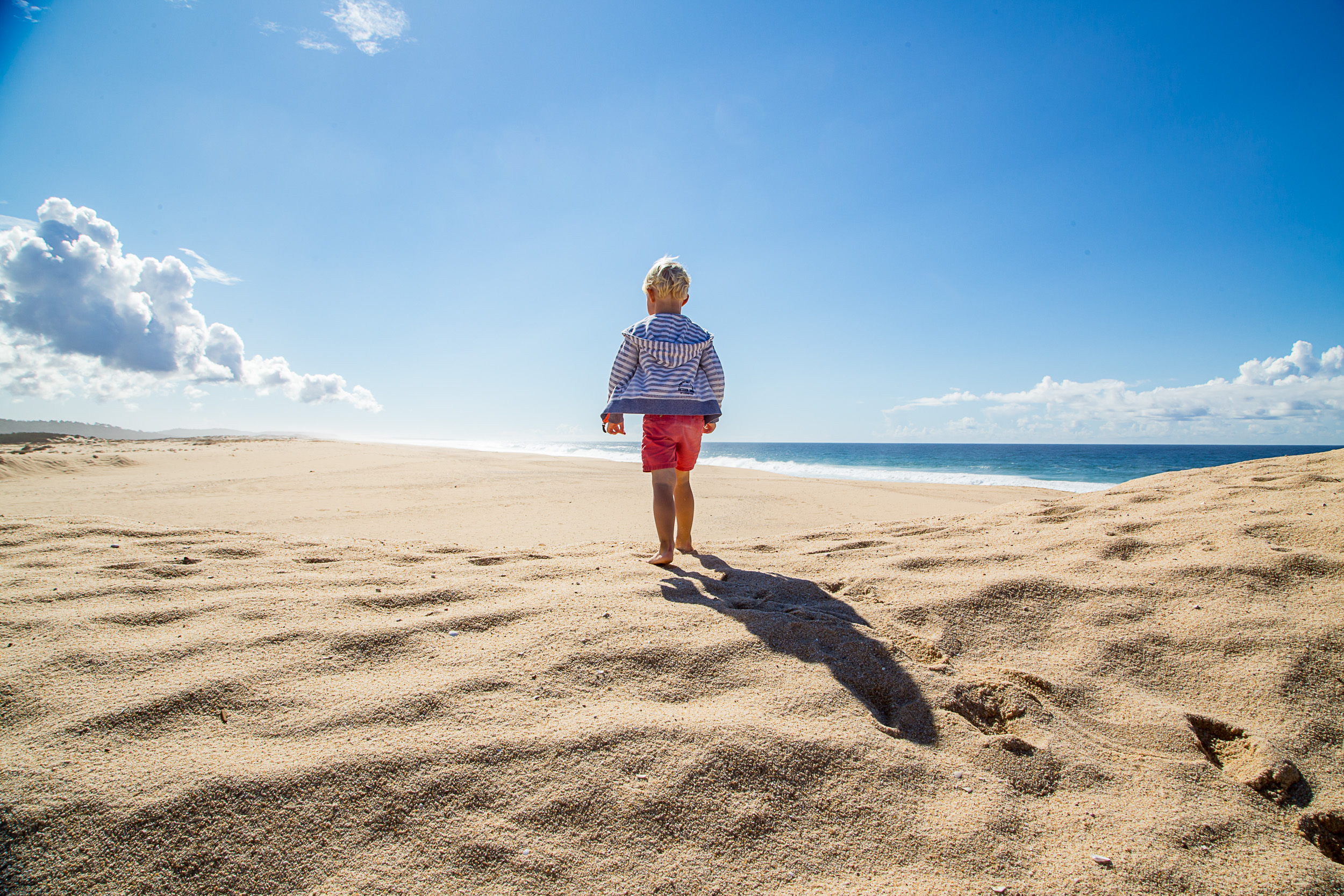 Ein einsames Kind blickt an einem weiten, menschenleeren Sandstrand in Comporta auf das blaue Meer