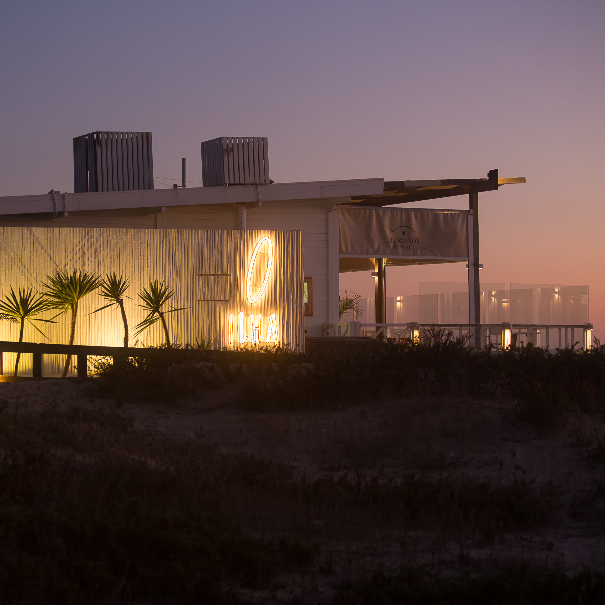 The illuminated Ilha neon sign at a stylish beach restaurant at dusk