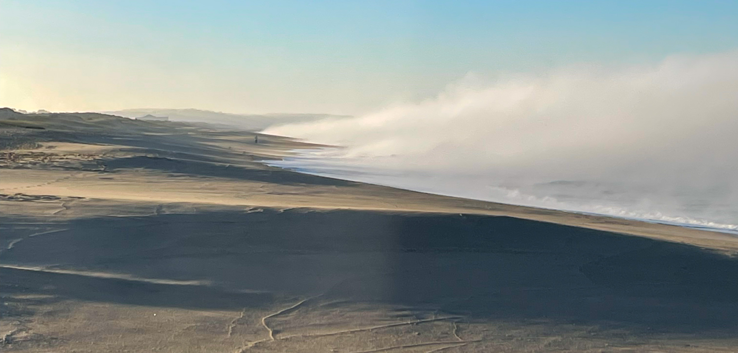 Vaste paysage de dunes sur la plage de Comporta, sur lequel un épais brouillard marin arrive de l'océan.