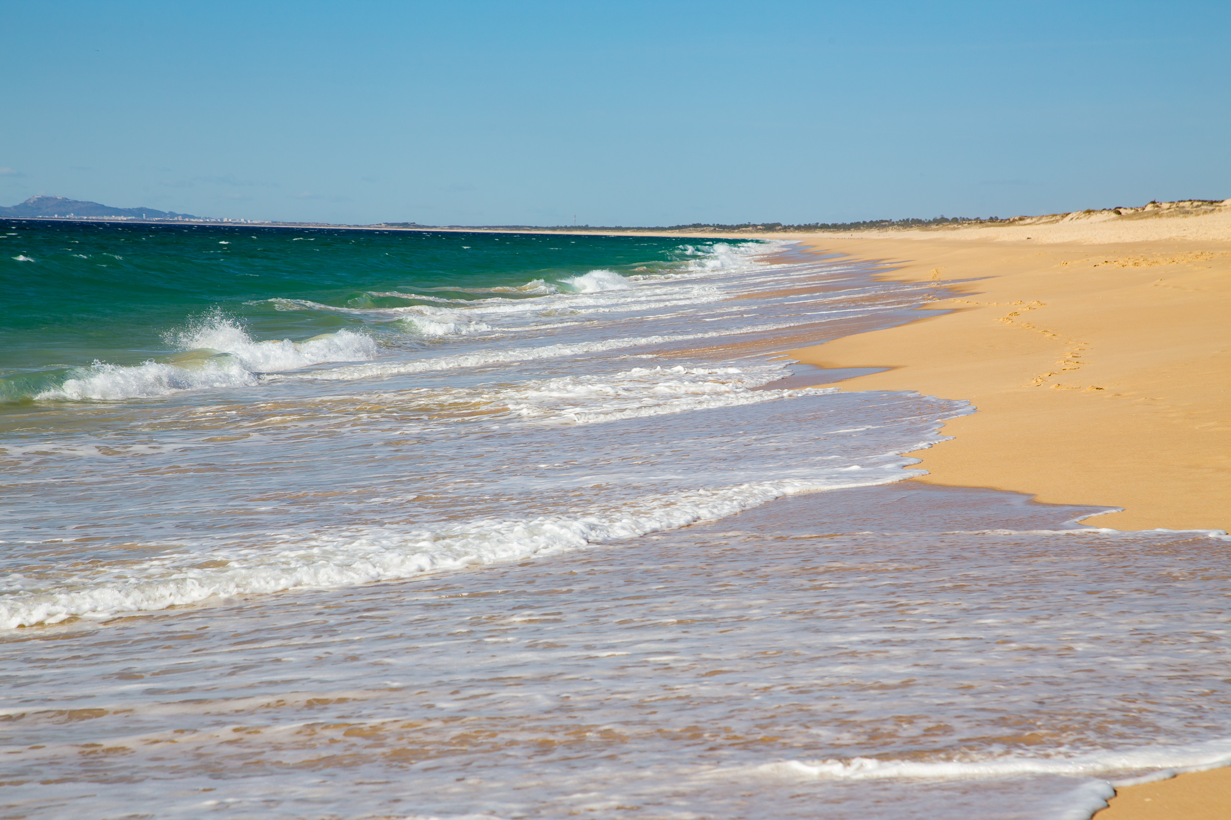 Vista ao longo da praia de areia infinita e vazia da Comporta com as ondas do Atlântico.