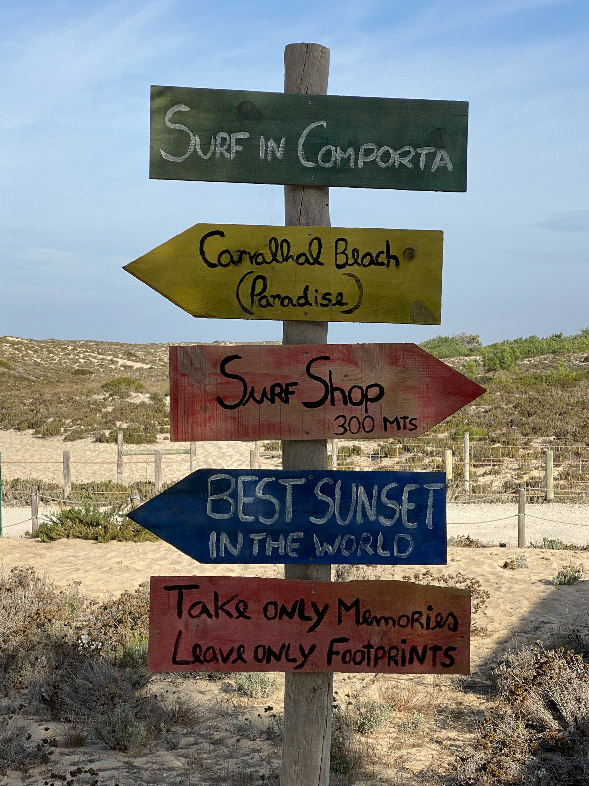 Un panneau indicateur en bois peint de couleurs vives à côté de la cabane en bois de l'école de surf Surf in Comporta.
