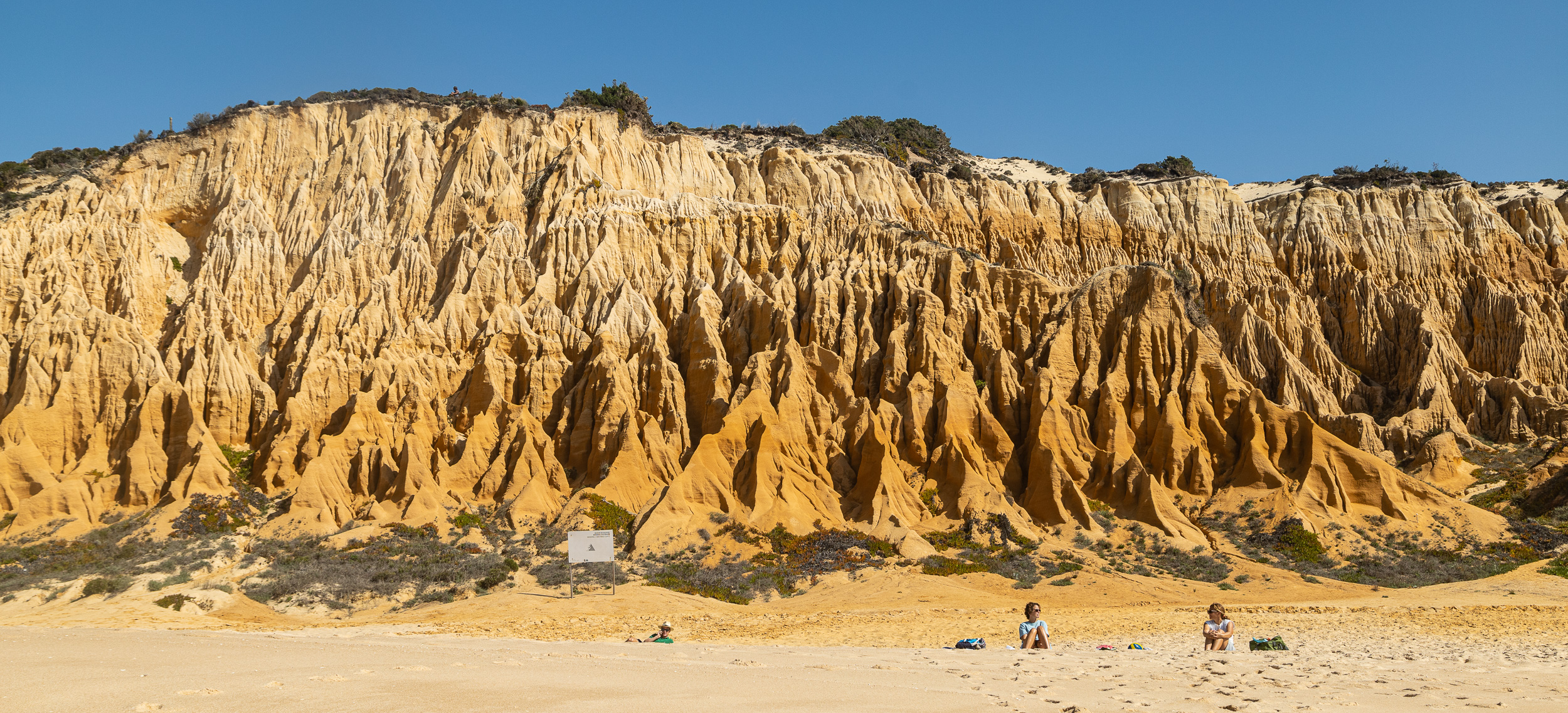 Des falaises fossiles monumentales d'un brun rouille s'élèvent à pic au-dessus de la plage de sable de Praia da Galé-Fontainhas, photographiées depuis la mer.