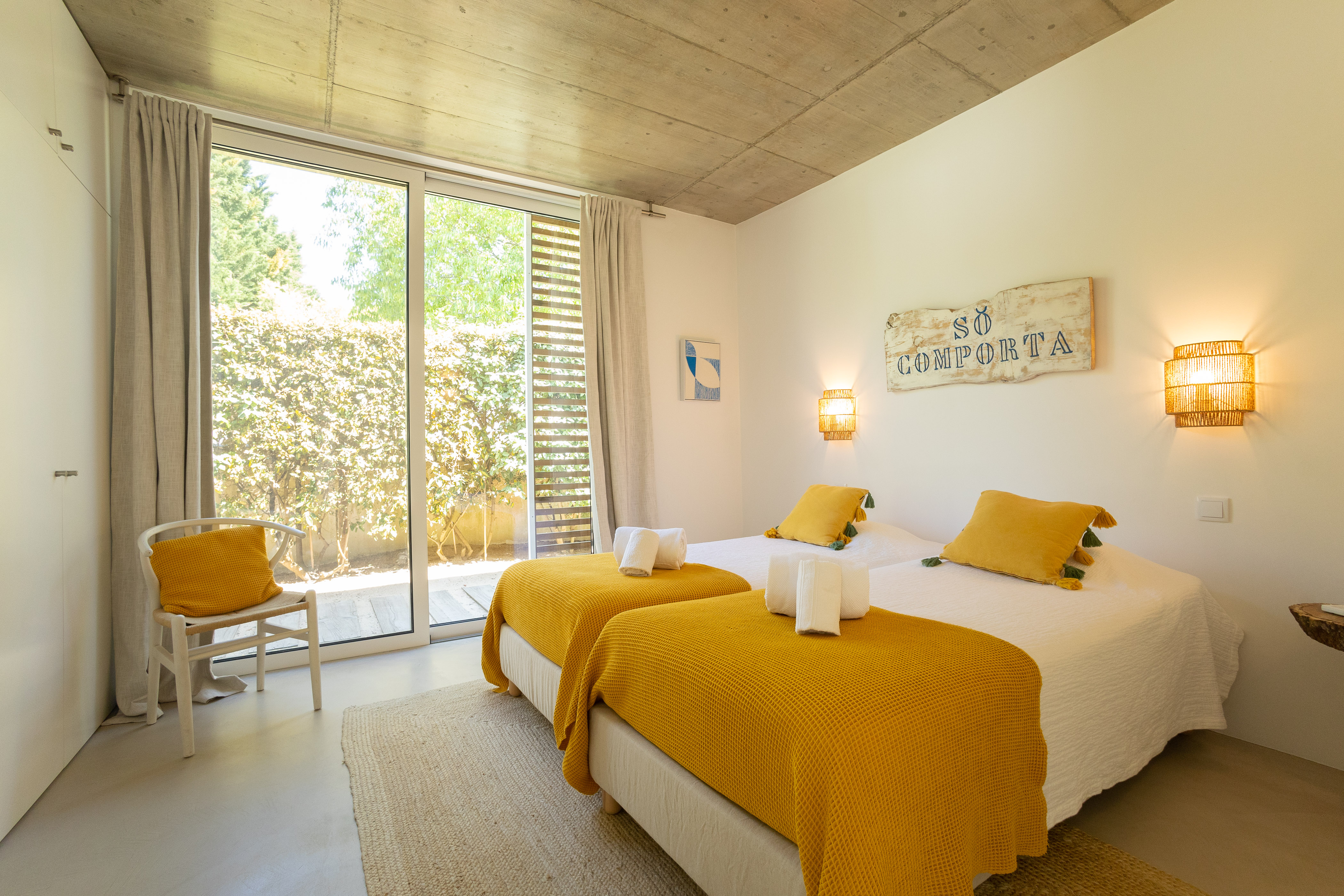 Ein gemütliches Doppelzimmer mit gelben Akzentkissen und einem 'Only-Comporta'-Holzschild