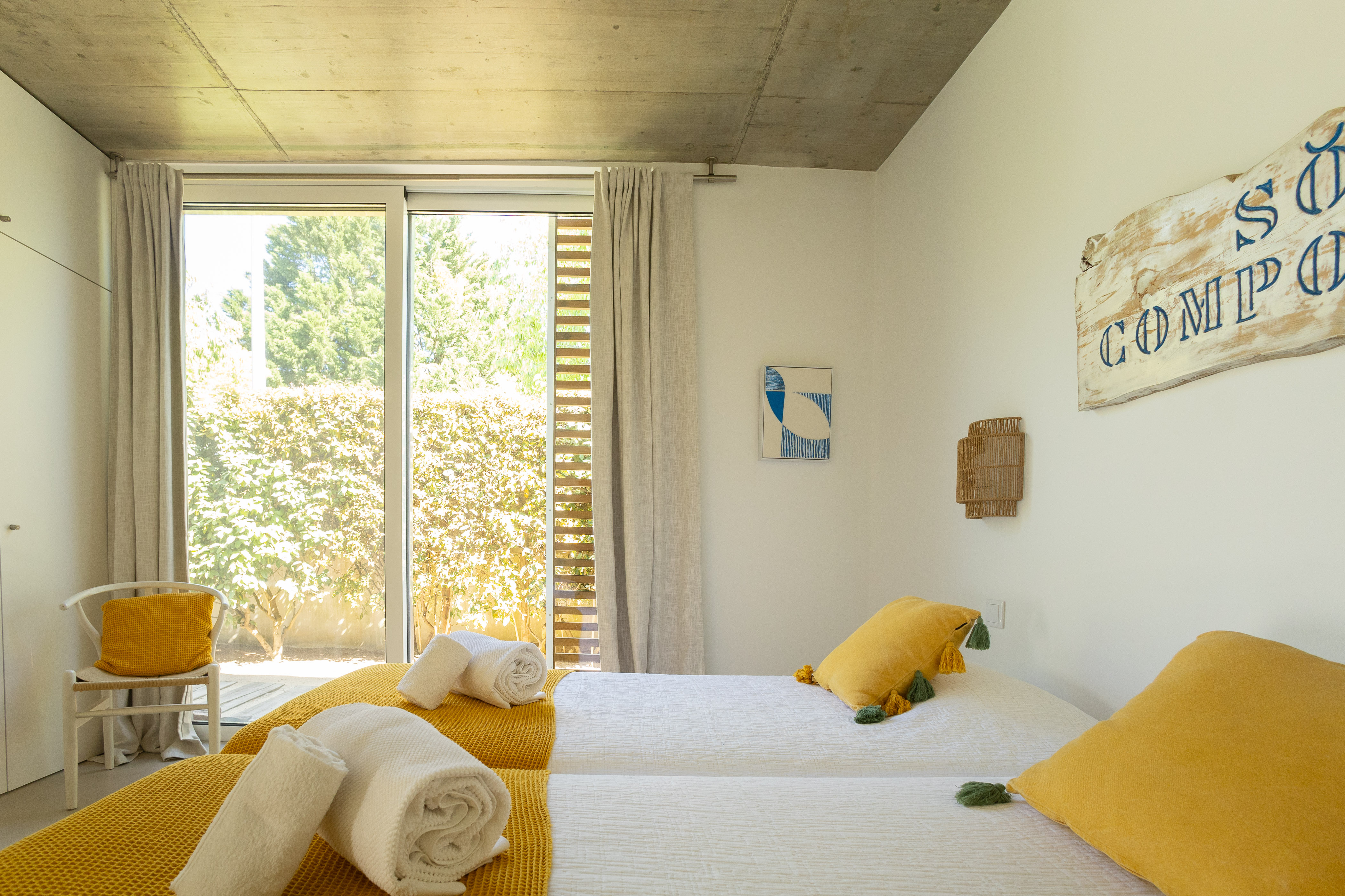 Ein helles Schlafzimmer mit gelben Kissen, einem Doppelbett und einem Surf-Wandbild