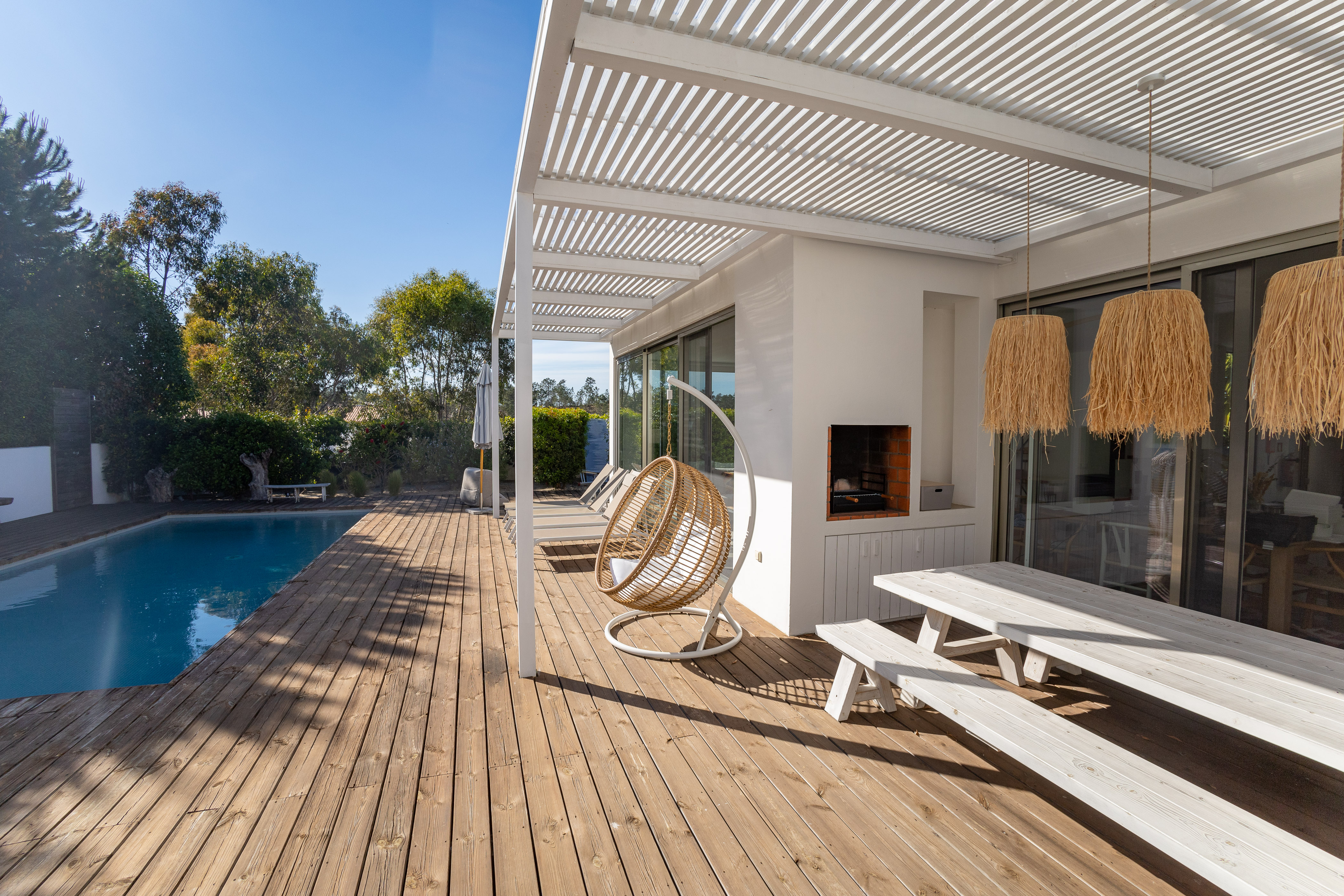 Blick entlang der sonnigen Holzterrasse mit gemütlichem Essbereich und angrenzendem Pool