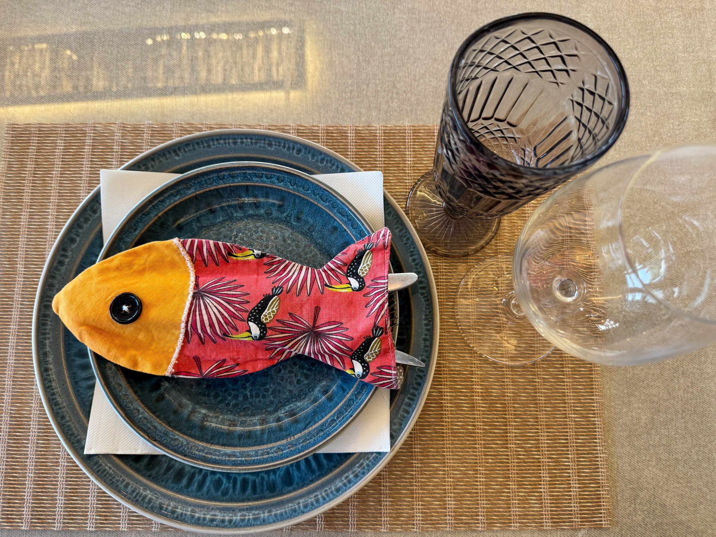 Ein liebevoll gedeckter Holztisch in einem Restaurant mit einer auffälligen Bestecktasche in Form eines Fisches.
