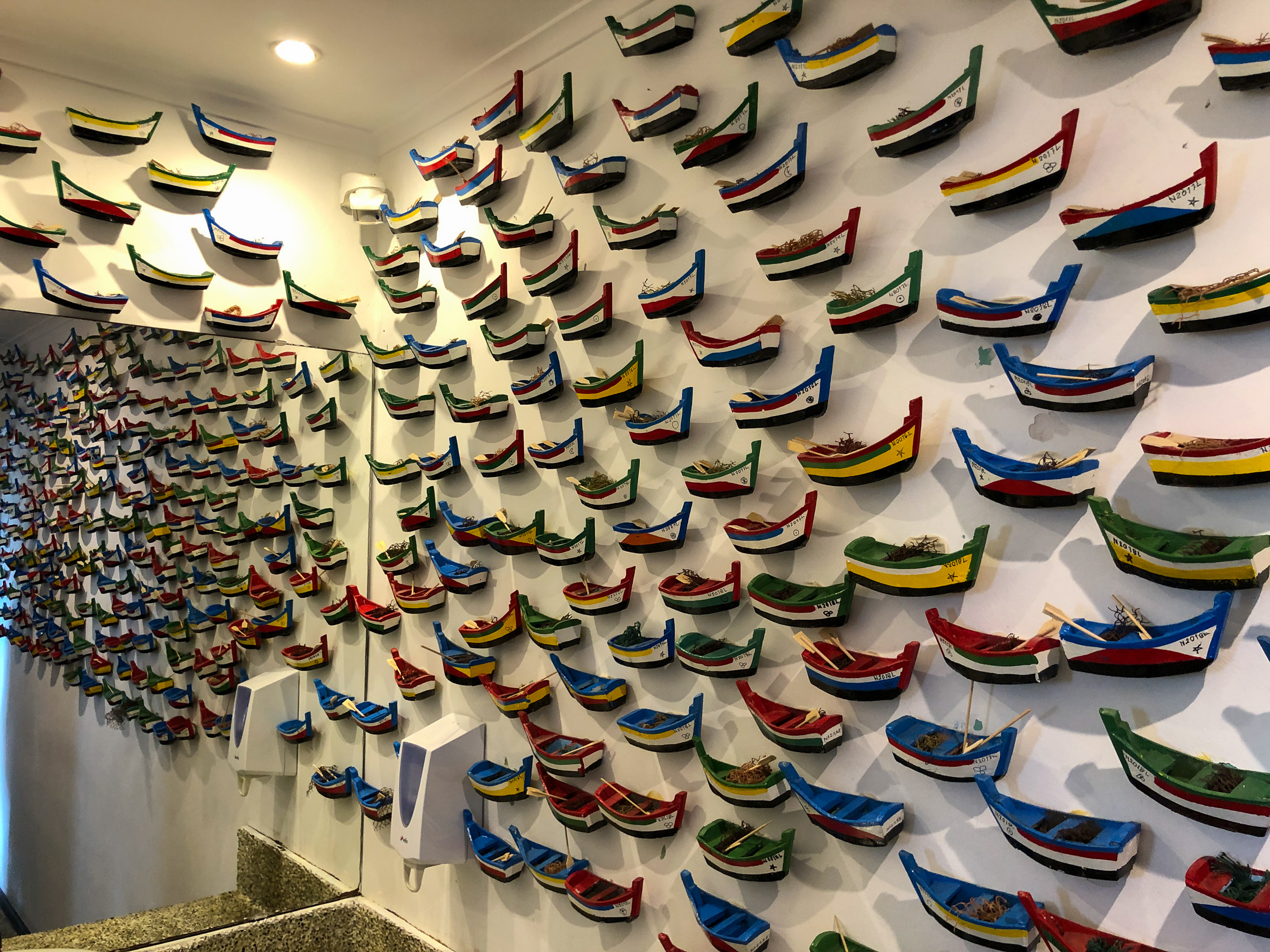 Eine weiße Wand, die vollständig mit bunten Fischtellern dekoriert ist.