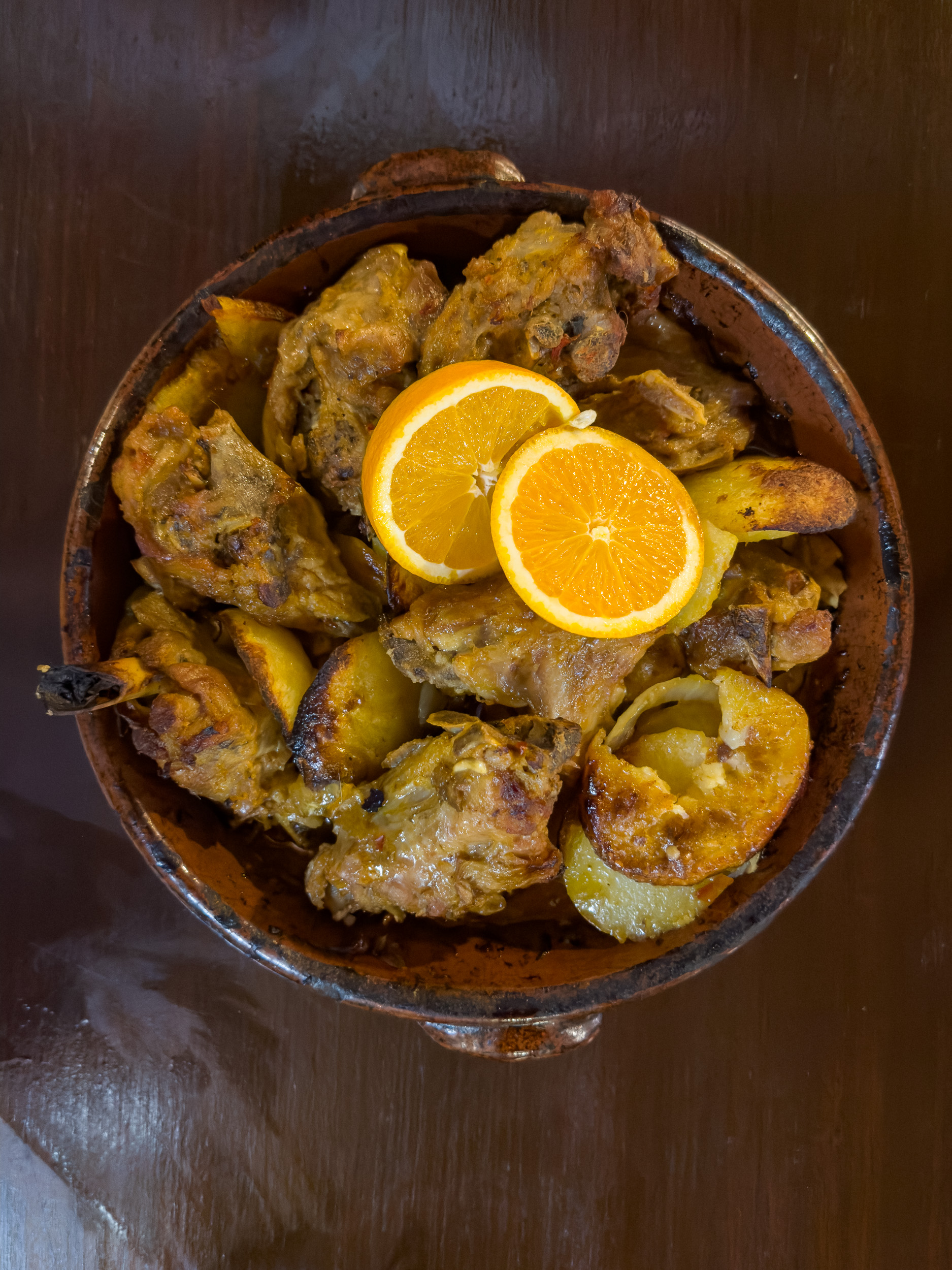 Un plat en terre cuite traditionnel avec du chevreau rôti croustillant et des pommes de terre sautées.