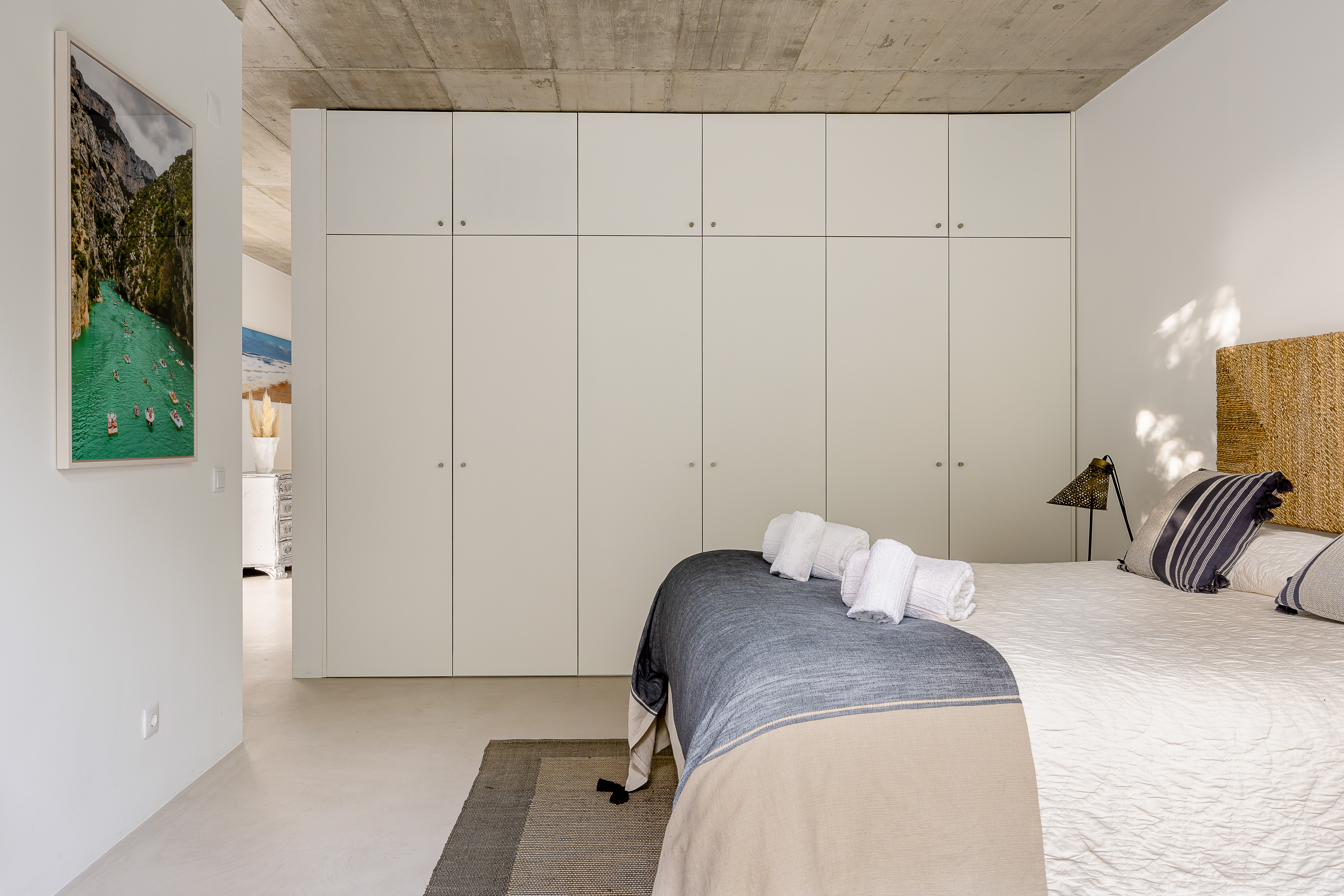 Ein helles Schlafzimmer mit Doppelbett, großen Einbauschränken und sichtbarer Betondecke