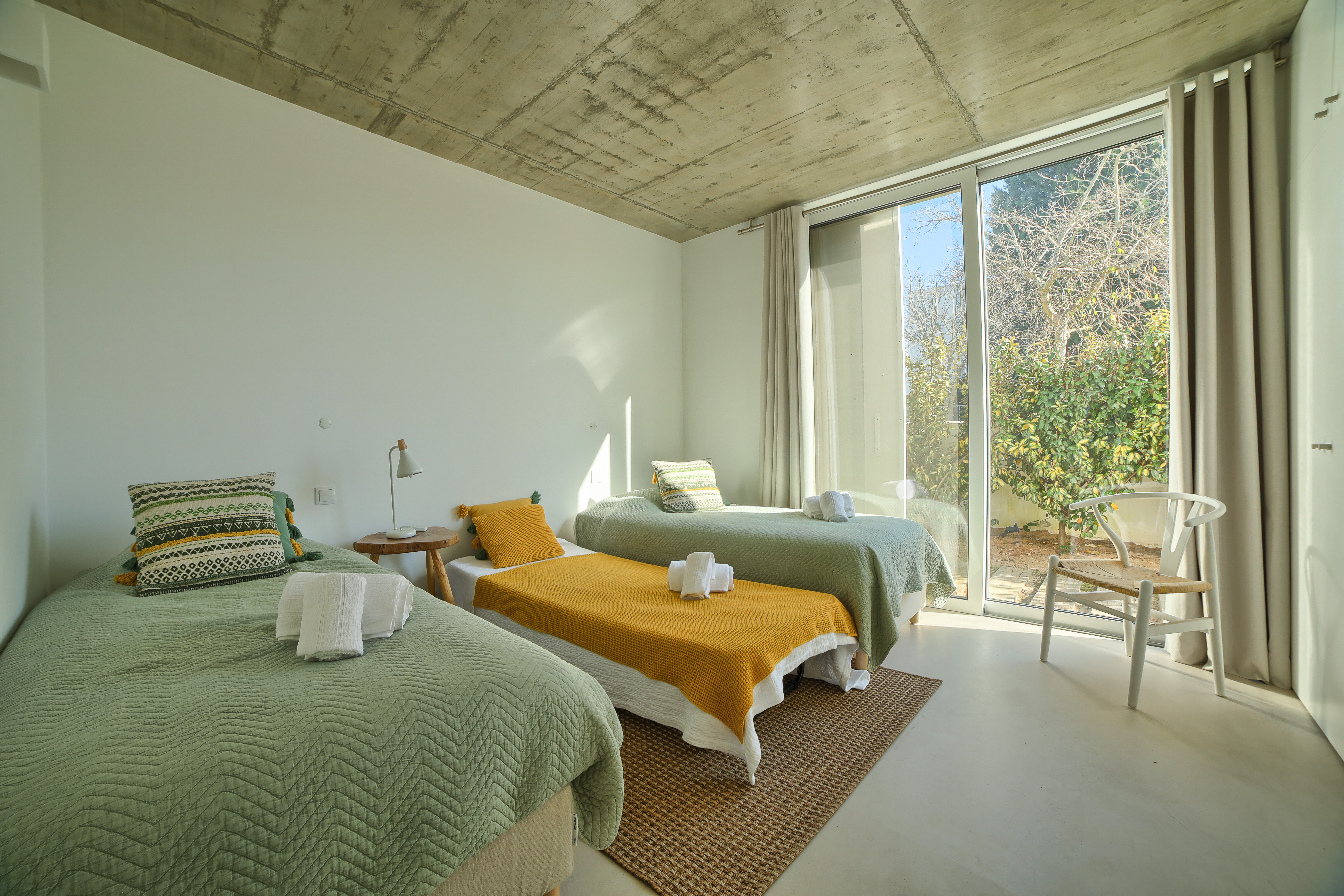 Ein Schlafzimmer mit zwei Einzelbetten und gemütlichen grünen Kissen vor Sichtbetonwänden