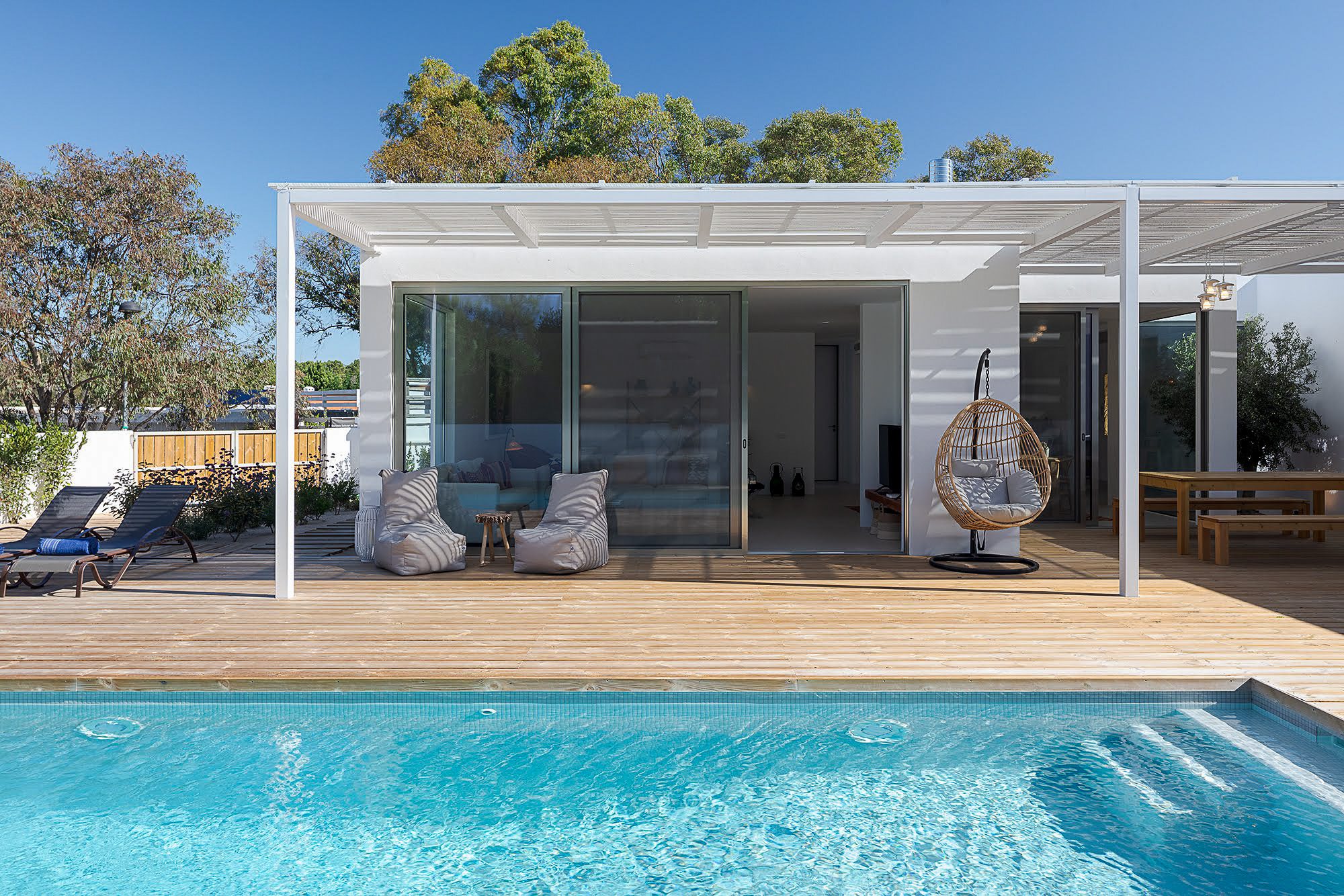 View across the blue swimming pool to the modern, white-designed Villa Laranjeiras with open glass fronts in the Alentejo - Life in the Sands